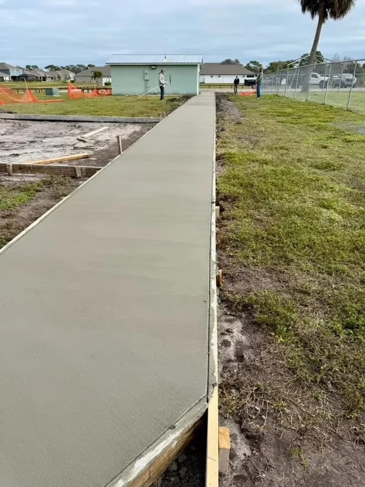 Fresh concrete walkway beside a fenced recreation area