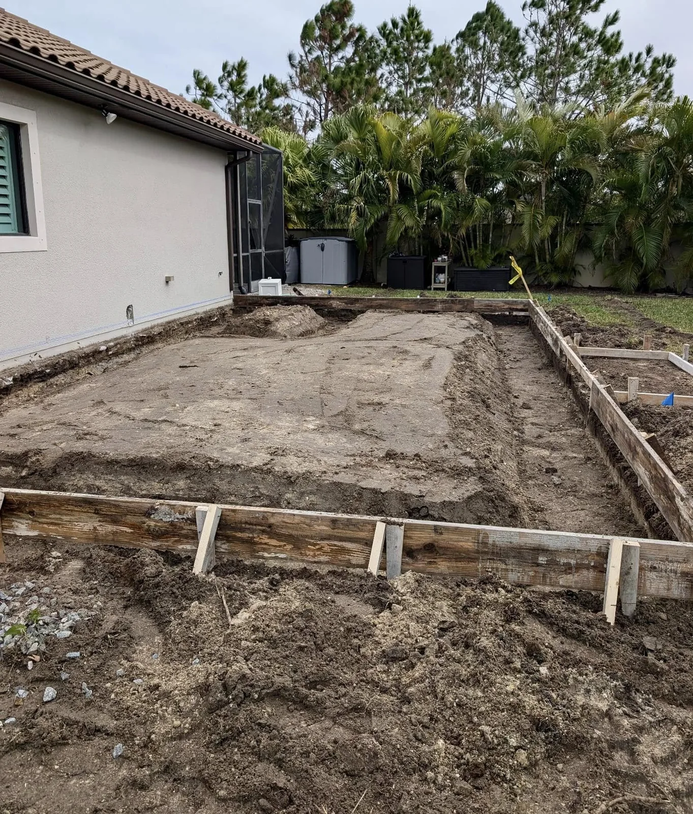 Excavated residential foundation area prepared beside an existing home by JCD Concrete