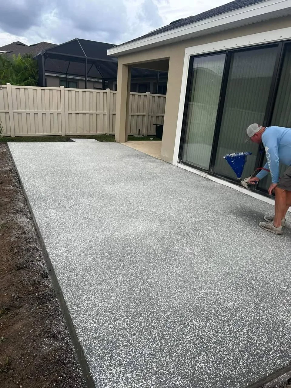 JCD crew member applying a spray-deck finish with a hopper to a back patio